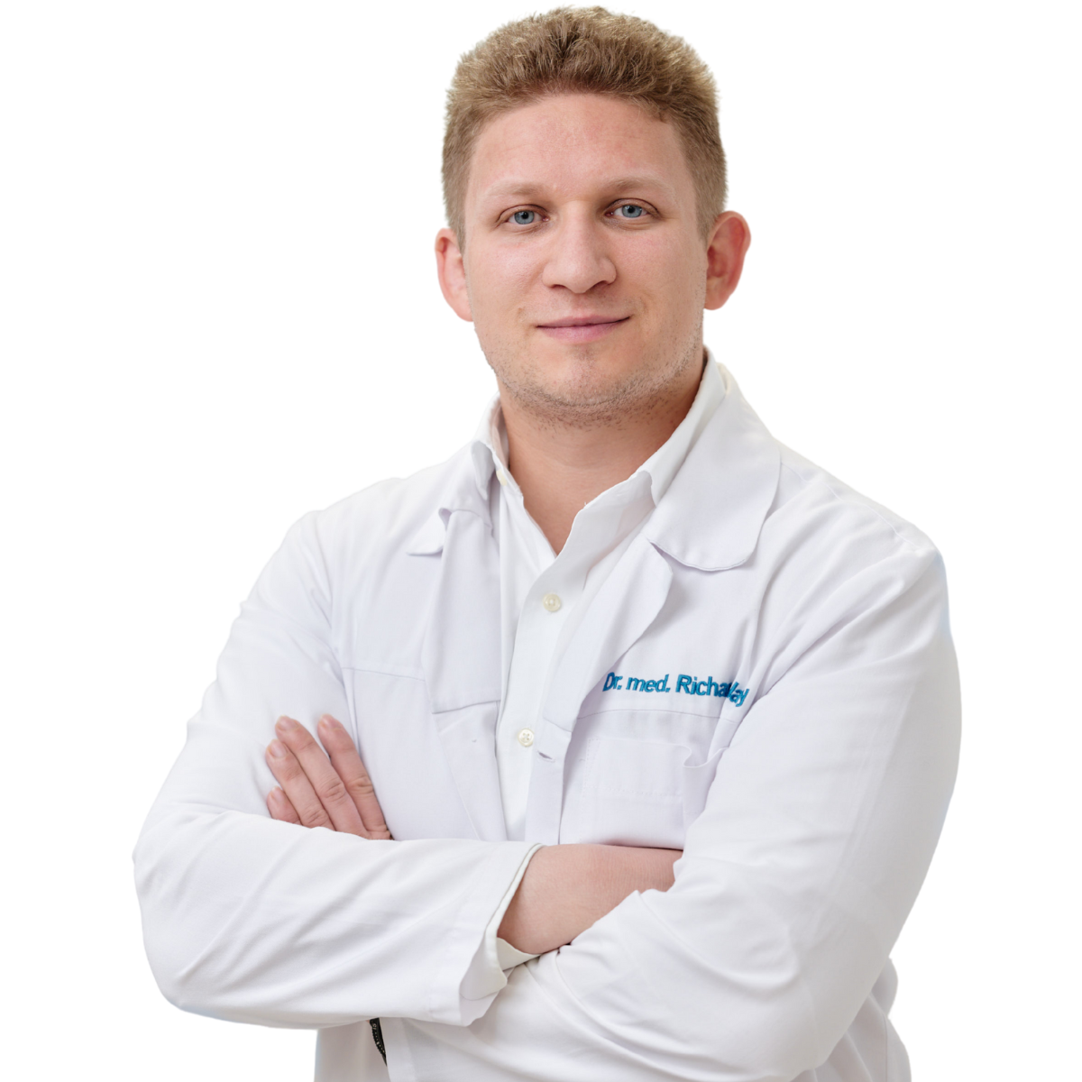 Ein Mann mit kurzen, lockigen, blonden Haaren trägt einen weißen Arztkittel mit der Aufschrift „Dr. med. (H) Richard Nagy“. Er steht mit verschränkten Armen vor weißem Hintergrund.
